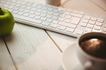 Keyboard with coffee and green apple on table