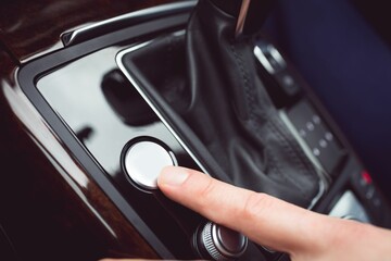 White finger pressing a small white button on a gear shift in a car