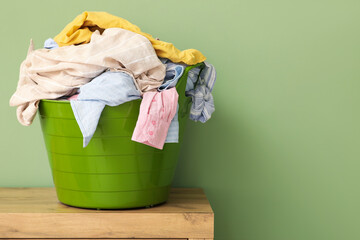 Basket with laundry on chest of drawers near green wall