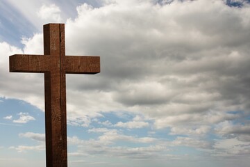 Wooden cross standing against cloudy sky in flat design, highlighting rough-hewn texture
