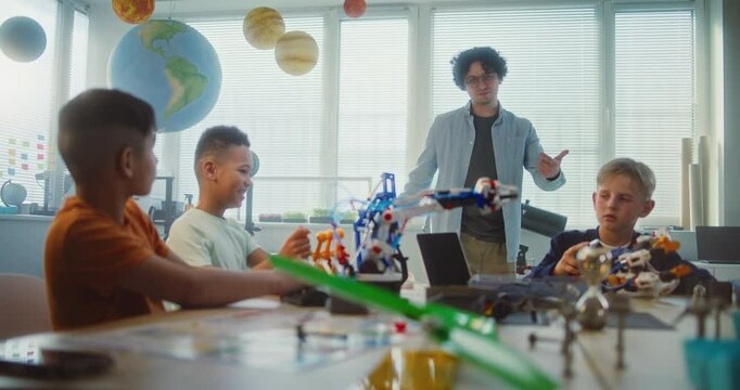 Young Teacher and Kids Doing Team Huddle Gesture in Multiethnic Classroom. Primary School Children Exploring Robotics and Renewable Energy Models, Celebrating Teamwork. STEM Learning. Slow Motion.