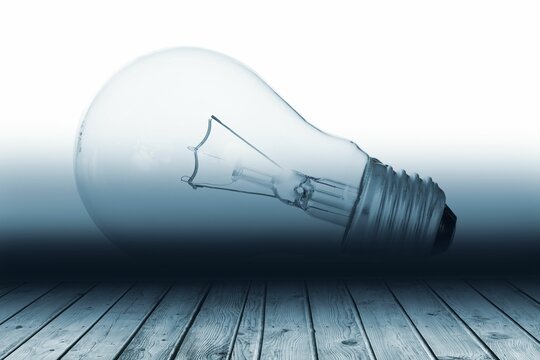 Fototapeta Incandescent light bulb is lying on weathered plank with blue gradient backdrop in flat design