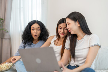 Diverse group of women friends smiling and talking while using laptop, browsing social media,...