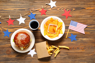 Tasty burger with flag of USA, french fries, potato chips and cola on wooden background. American...