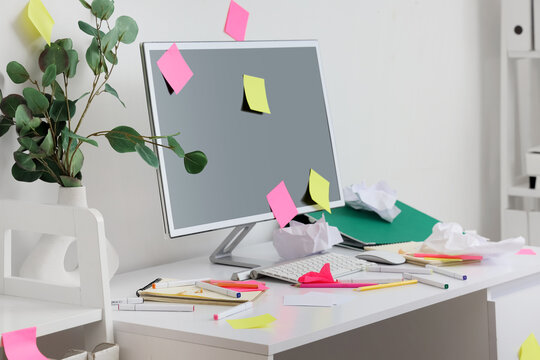 Messy workplace with computer monitor and sticky notes in light office