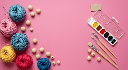 Craft supplies on pink colorful yarn, wooden beads, watercolor paints, brushes. Essential art and craft materials for creative hobbies, DIY projects.