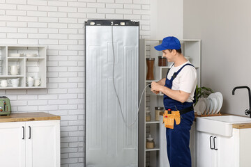 Happy male worker repairing refrigerator in kitchen