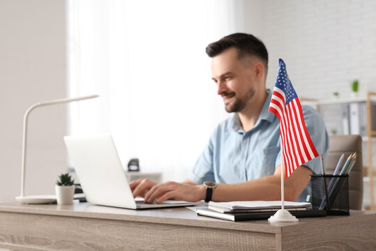 Handsome young happy man with laptop and flag of USA working at table in office - Powered by Adobe