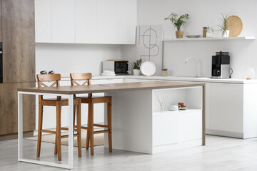 Interior of light kitchen with modern island table and white counters