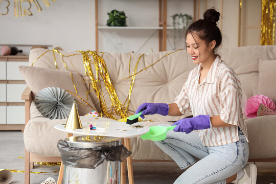 Young Asian woman sweeping confetti from table at home after Birthday party - Powered by Adobe