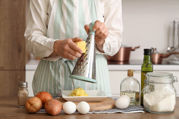 Woman grating potato at table in kitchen, closeup