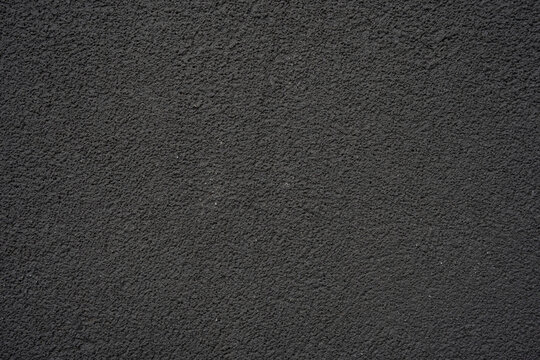 A dark, rough, and granular textured surface, resembling asphalt, coarse concrete, or stucco. Ideal as an abstract background, providing a solid and rugged feel for various design projects.