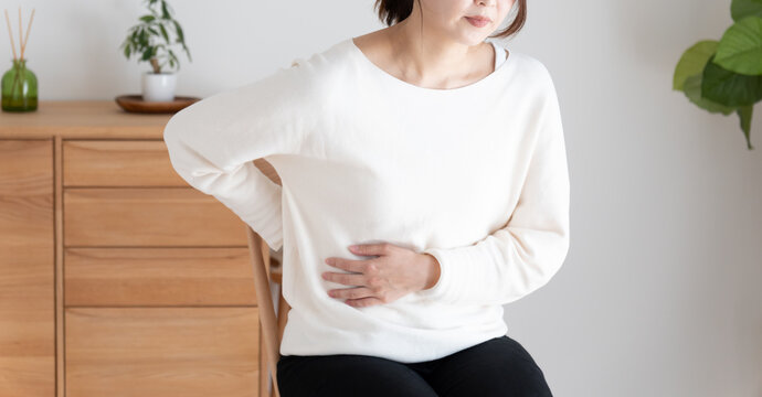 お腹と背中を押さえる体調不良の女性