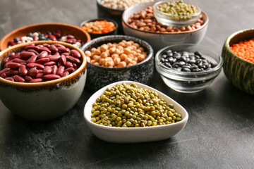 Fototapeta premium Bowls of different raw legumes on dark background