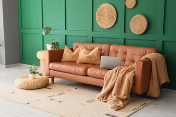 Interior of living room with wicker ottomans, houseplants and laptop on stylish leather sofa near...
