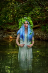 A mermaid with blue hair in a white dress stands in the river