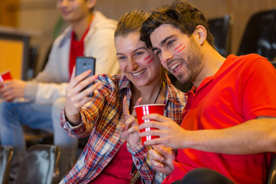 couple of supporters watching football game and making selfie