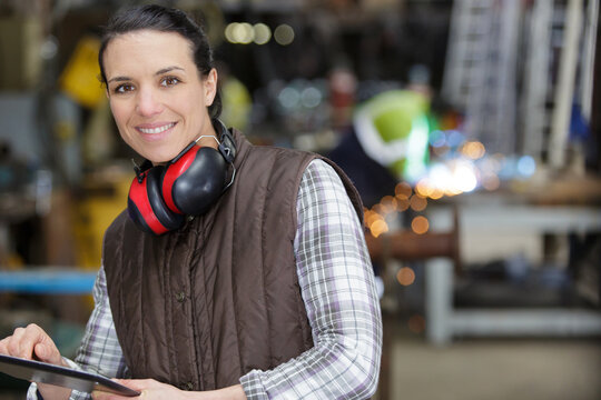 portrait of young female carpenter wearing ear protectors in workshop - Powered by Adobe