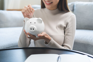 Saving money wealth concept, asian young business woman hand putting coin into piggy for saving...