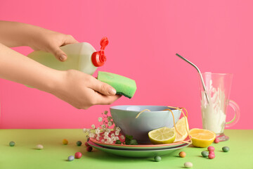 Female hands with dirty dishes, detergent and sponge on color background