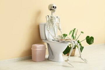 Human skeleton with magazine sitting on toilet bowl in restroom