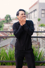 Young man in black shirt experiencing pain holding face with hands on a building rooftop