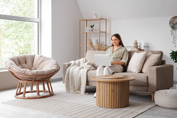 Beautiful young woman using laptop on cozy grey sofa in stylish living room