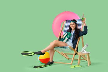 Young businesswoman with cocktail and folders in deck chair on green background. Summer vacation...