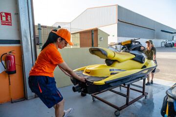 Mechanics moving personal watercraft on a cart in repair shop