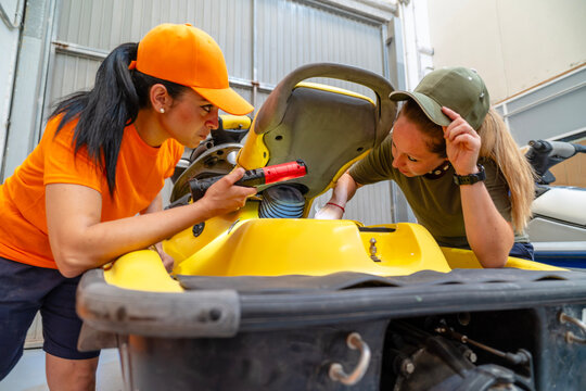 Two female mechanics repairing personal watercraft engine in workshop
