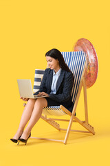 Young businesswoman using laptop in deck chair on yellow background. Summer vacation concept