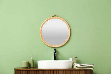 Stylish mirror hanging on green wall over wooden cabinet with sink in bathroom