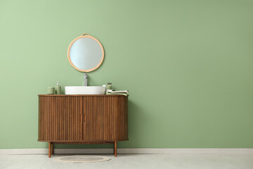 Stylish mirror hanging on green wall over wooden cabinet with sink in bathroom