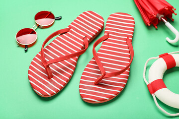 Composition with stylish flip-flops, sunglasses and decorative lifebuoy on green background, closeup