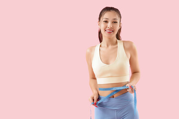 Sporty young Asian woman measuring waist on pink background. Diet concept