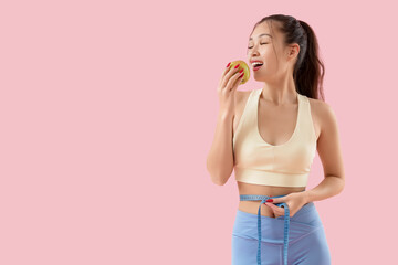 Sporty young Asian woman with apple measuring waist on pink background. Diet concept