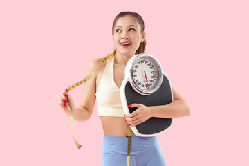Sporty young Asian woman with tape measure and weight scales on pink background. Diet concept
