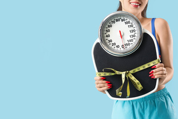 Sporty young woman with weight scales on blue background. Diet concept