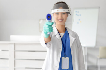 Female medical intern in protective mask with infrared thermometer at hospital