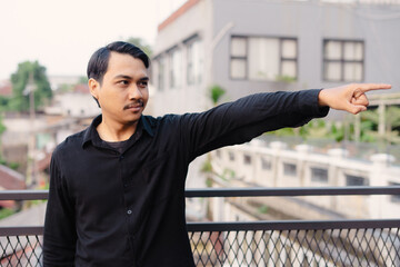 Man in Black Shirt Pointing Towards Direction with City Background, Outdoor Scene