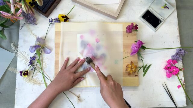 Botanical hammer art in action &ndash; flower pigments visible through parchment, wooden hammer resting on top during floral printmaking process