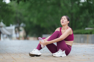 Asian woman suffering from ankle pain while exercising in a park