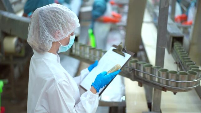 Quality control officer inspects a canned fish on the conveyer belt in factory.