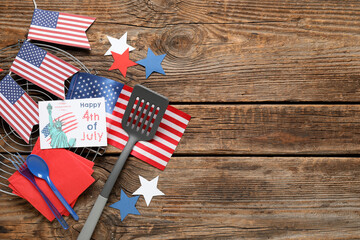 USA flags, greeting card with text HAPPY 4TH OF JULY and barbecue utensils on wooden background....
