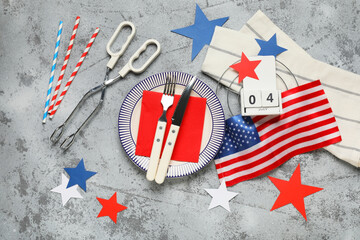 USA flag, calendar with date 04 JULY, dinnerware and barbecue tongs on grey grunge background....