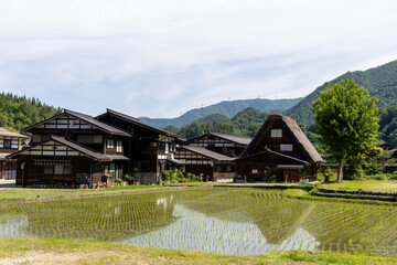 白川郷の合掌造り家屋や民家が水田に映り込む初夏の風景。青空と山並みが爽やかさを演出する田園風景。  © Jazz Hapi Yuko
