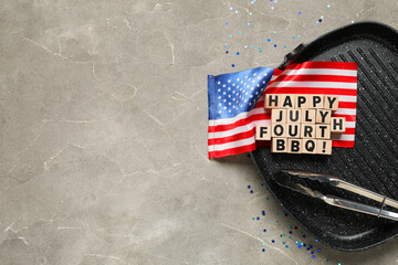Grill pan with USA flag, words HAPPY JULY FOURTH BBQ and barbecue tongs on grey grunge background....