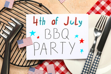 USA flags, greeting card with text 4TH OF JULY BBQ PARTY, dinnerware and barbecue tongs on beige...