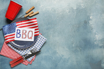 USA flag, card with word BBQ, dinnerware and barbecue skewers on blue grunge background....