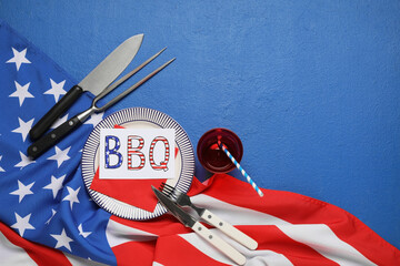 USA flag, greeting card with text HAPPY 4TH OF JULY, dinnerware and barbecue utensils on blue...